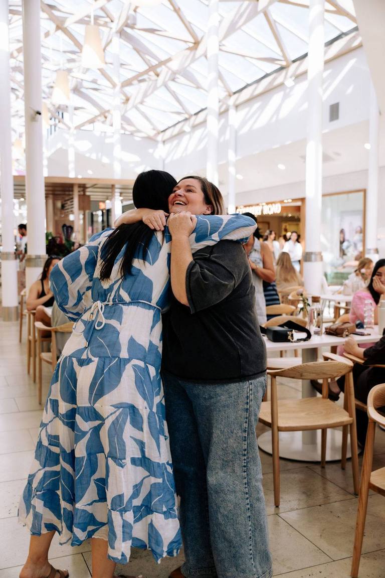 Two women in a big joyful hug at an Open Coffee event in an Adelaide cafe