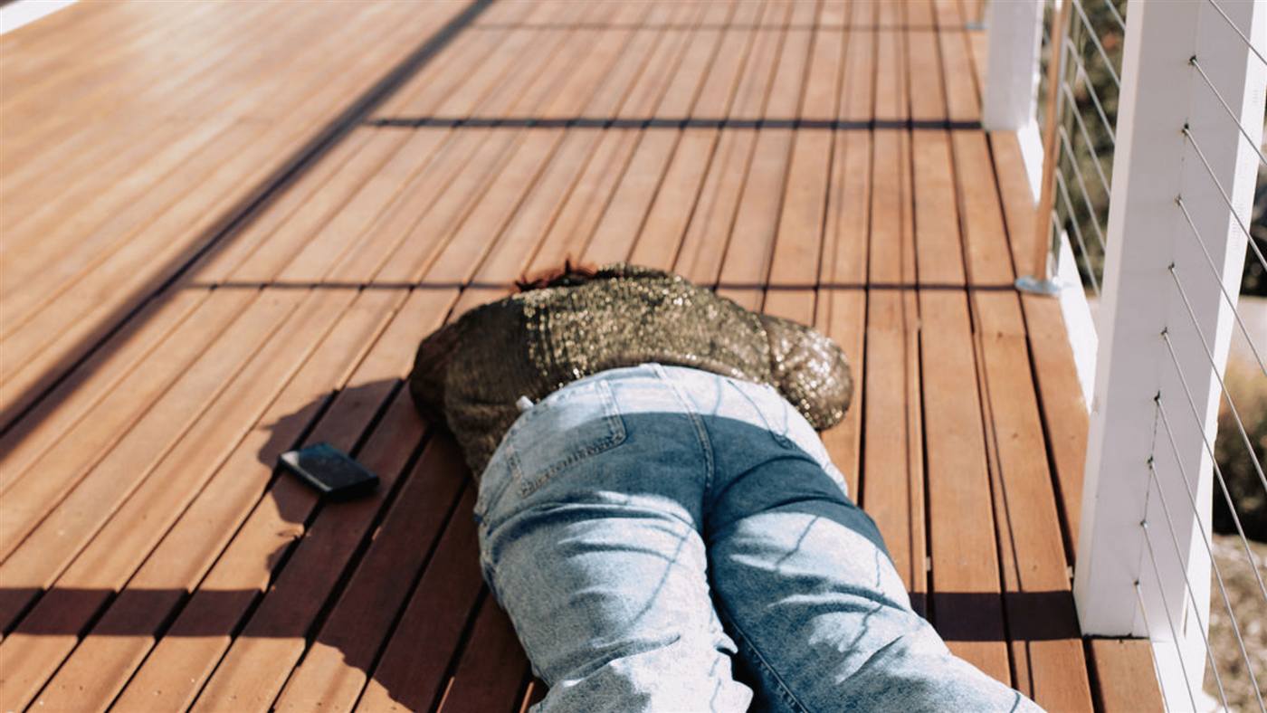 Sandra lying face down on a wooden deck, phone beside her