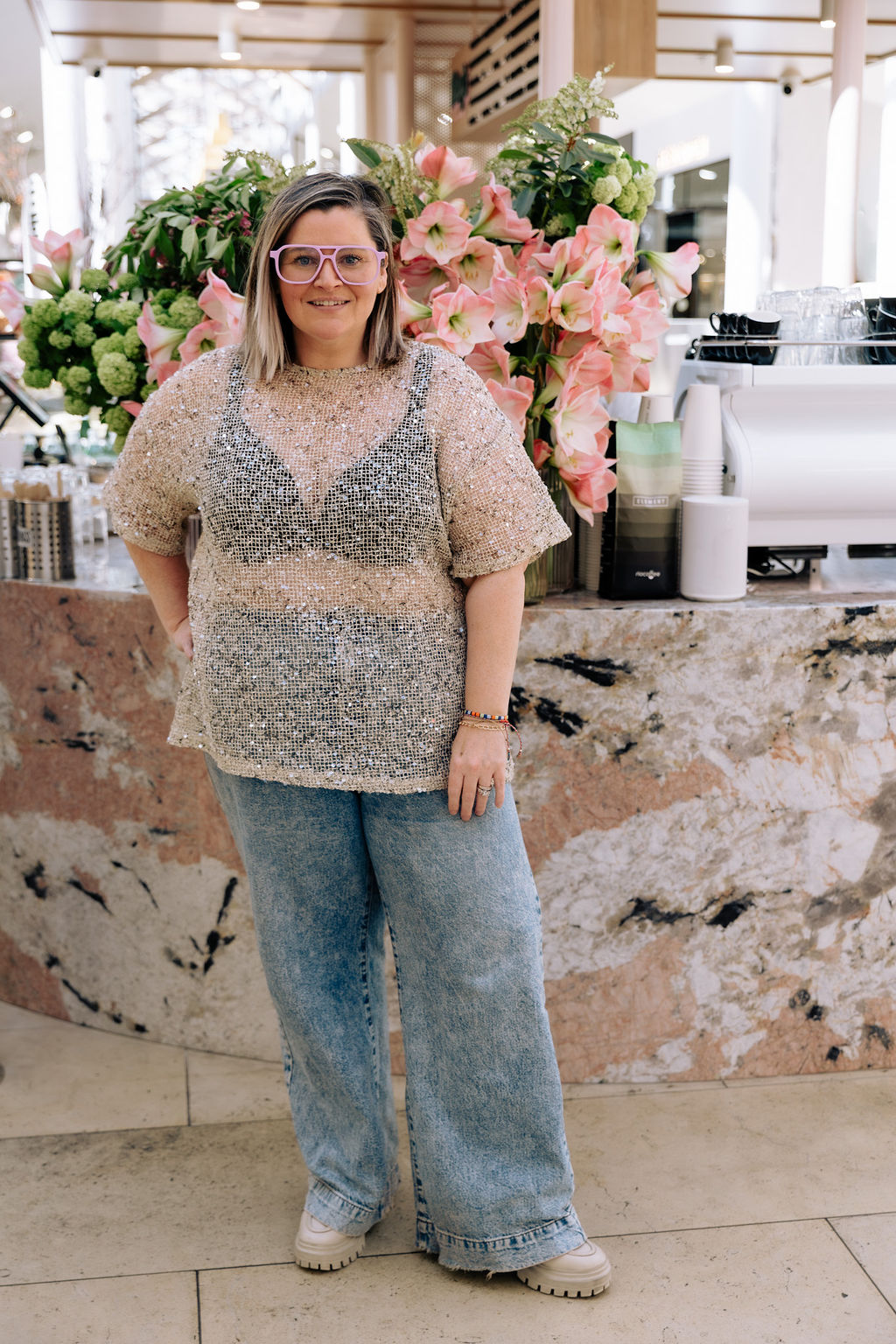 Sandra in a sequin top at a cafe counter in Adelaide, flowers behind her