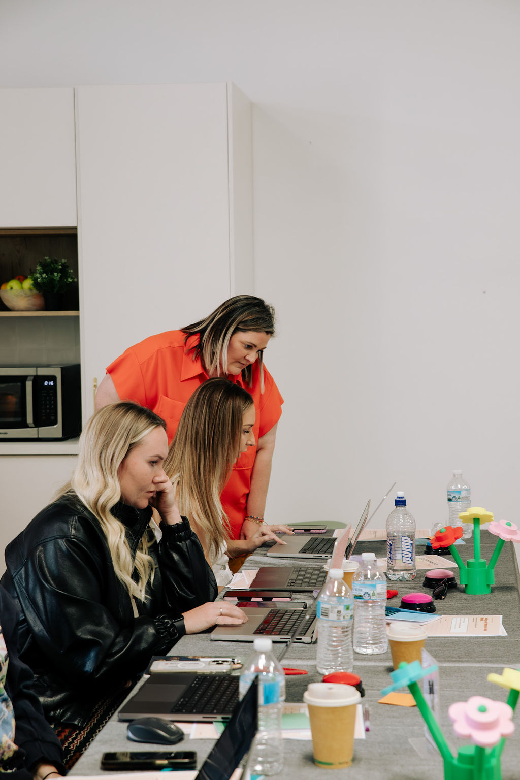 Sandra leaning over a laptop beside two women at the Claude Foundations day