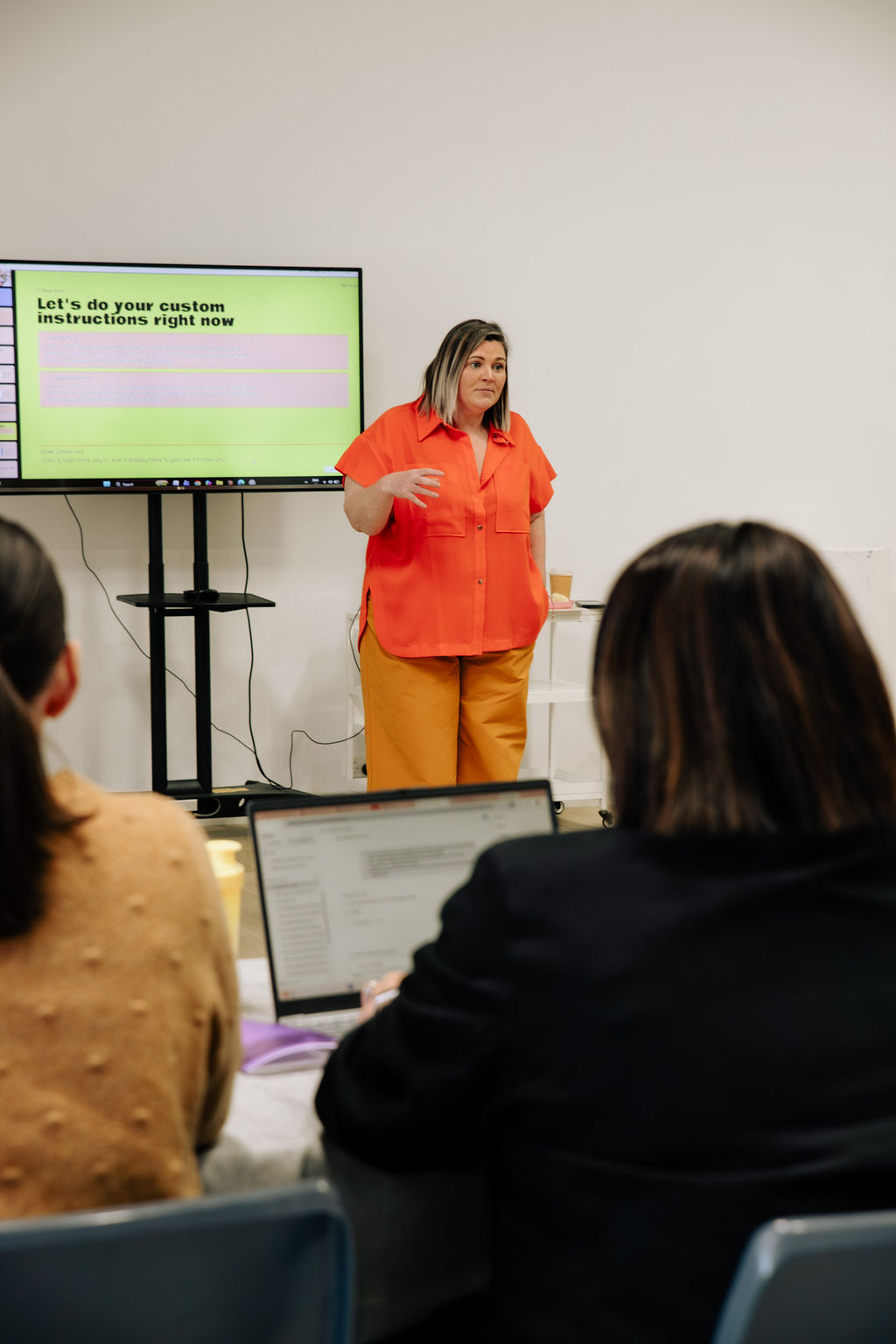 Sandra teaching at the screen, two women at laptops in the foreground