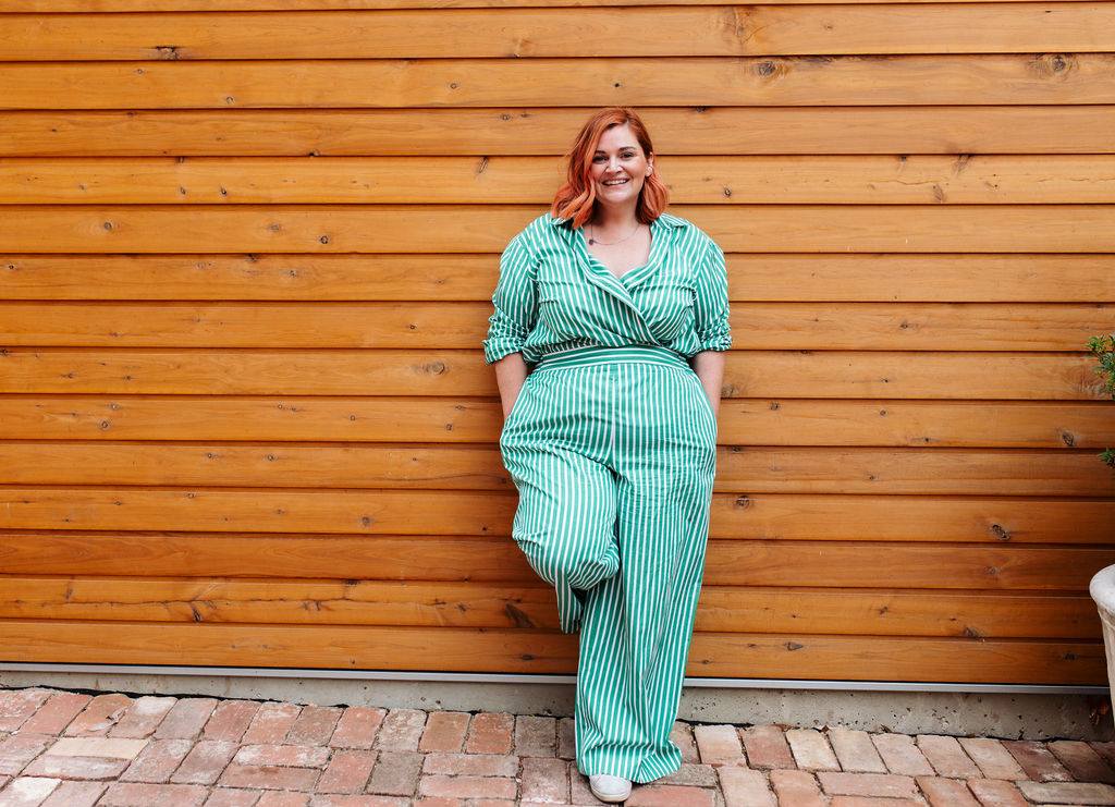 Woman in a green striped outfit leaning against a timber wall, smiling